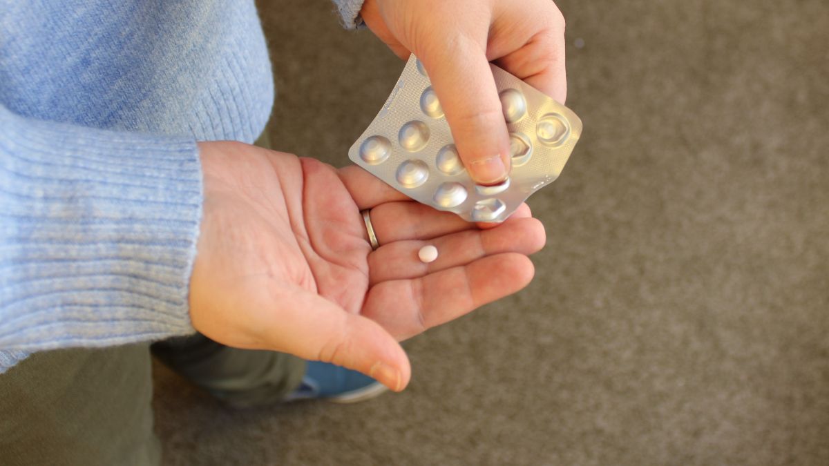 Osoba berie tabletku z blistra, čo symbolizuje užívanie antipsychotík.