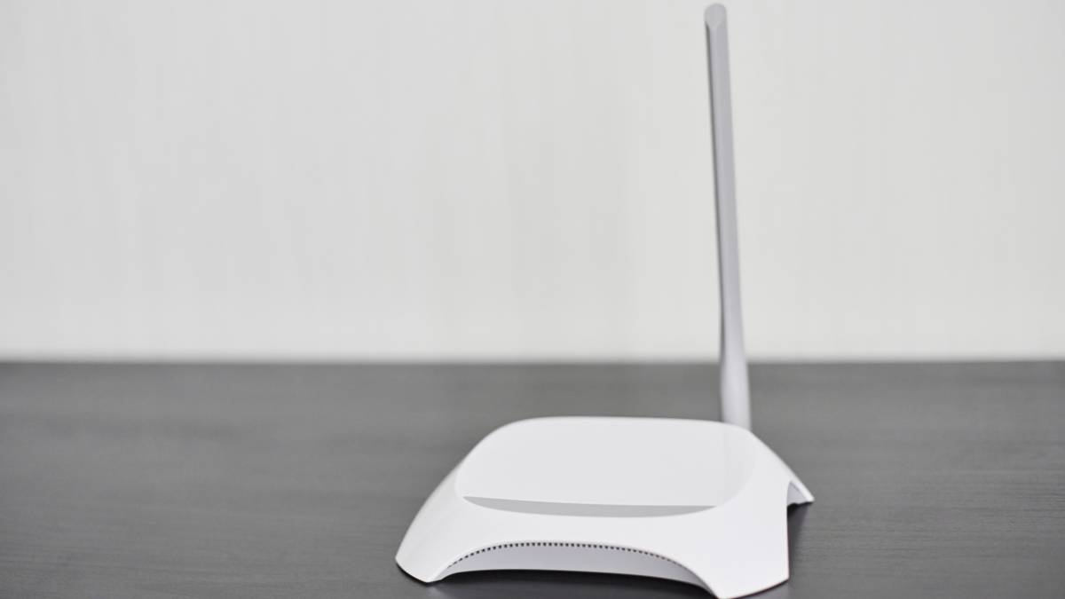 Biely router s anténou na tmavom stole, symbolizujúci sieťové pripojenie.