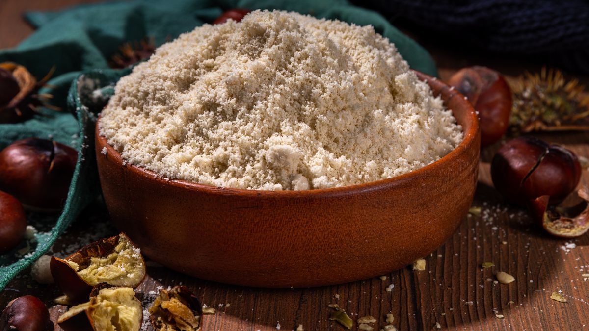 Miska plná gaštanovej múky obklopená gaštanmi a textíliou.