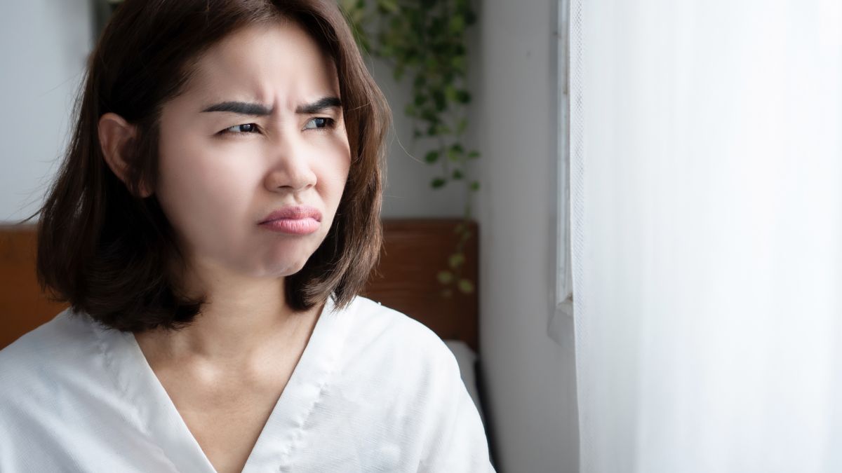 Žena s nahnevaným výrazom hľadí von oknom, vyjadruje frustráciu.