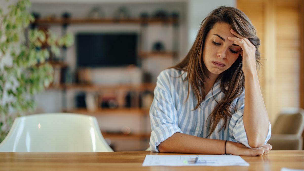 Žena s unaveným výrazom sedí pri stole, premýšľa o svojich myšlienkach.