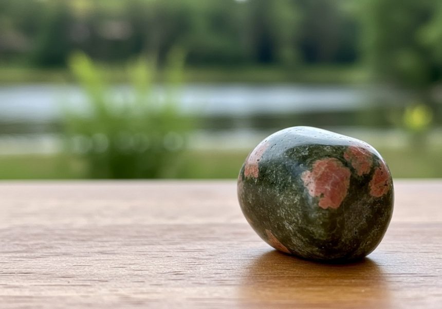 Unakit kryštál s jemnými ružovými a zelenými odtieňmi, na drevenej ploche.