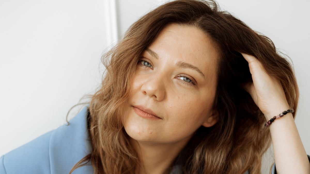 Žena s dlhými vlnitými vlasmi sa usmieva a pozera sa do objektívu.