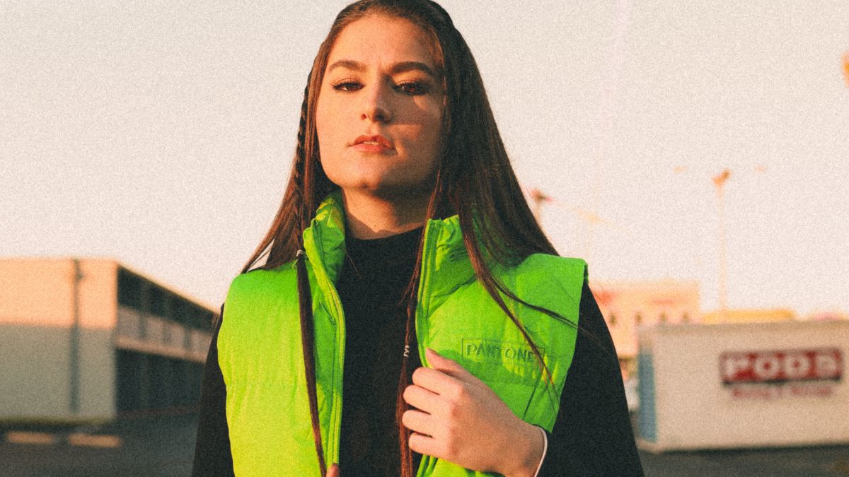 Mladá žena v jasne zelenej veste, s dlhými vlasmi a elegantným výrazom.