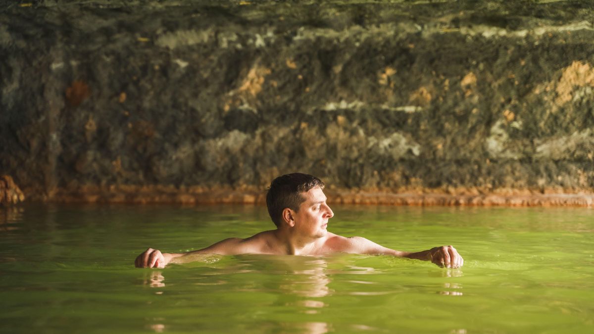 Muž relaxuje vo termálnej vode s minerálnymi zložkami v prírodnom prostredí.
