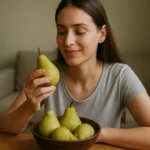 Žena drží hrušku s úsměvem, vedle mísa plná hrušek.