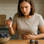 Žena so slivkou v ruke, vyzerá nepokojne, drží sa za brucho.