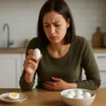 Žena s vajcom a bolesťou brucha vedľa taniera s vareným vajcom