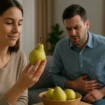 Žena skúma hrušku, muž má bolestivý výraz kvôli nadúvaniu.