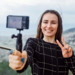 Mladá žena robí selfie s kamerou na pozadí mestského panorámu.