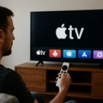 Muž ovládajúci Apple TV pomocou diaľkového ovládania a sledovanie obrazovky.