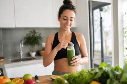 Žena s pohárom zeleného smoothie v moderne zariadenej kuchyni.