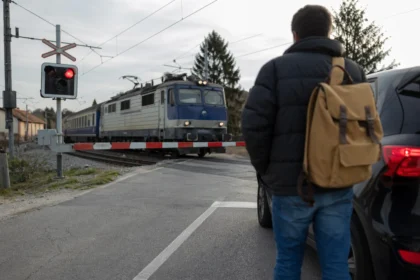 Osoba čaká pred železničnými závorami a prichádza vlak.