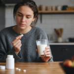 Žena s pohárom mlieka a liekom, hodnotí interakciu mlieka a liekov.