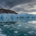 Rozsiahly ľadovec s odtávajúcimi kryhami na pozadí hmlistých oblakov.