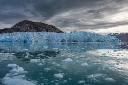 Rozsiahly ľadovec s odtávajúcimi kryhami na pozadí hmlistých oblakov.