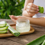 Aloe vera gel being applied to skin with fresh leaves on a wooden table