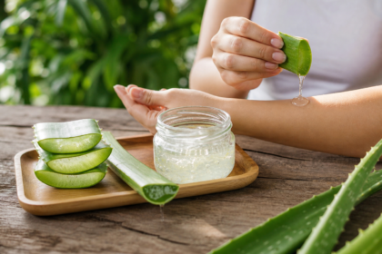 Aloe vera gel being applied to skin with fresh leaves on a wooden table