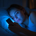 Žena sleduje mobilný telefón vyžarujúci modré svetlo v noci.
