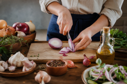 Žena krája cibuľu na doske s bylinkami a sezónnymi ingredienciami
