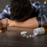 Muž so sklopenou hlavou, pohár s alkoholom a lieky na stole