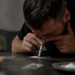 Muž užívajúci kokaín na stole s drogou.